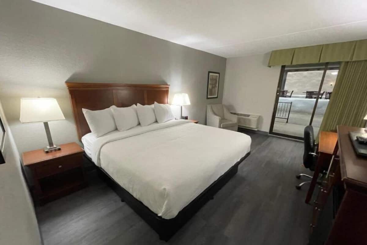 A hotel room with a large bed, two bedside tables with lamps, a chair, a desk, and a view of the outside through a large window.