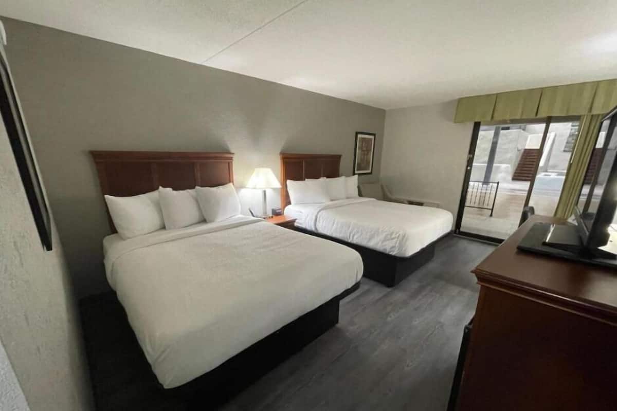 A hotel room with two beds, a desk, and a window with a view.
