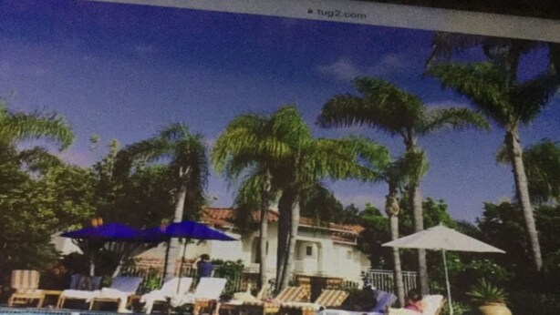 A swimming pool with lounge chairs and umbrellas, surrounded by palm trees and a building with a tiled roof. - Beautifully situated above the Pacific within a tranquil natural sactunctuary. (Carlsbad)
