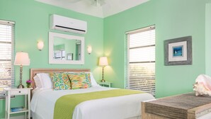 Een slaapkamer met een bed, twee nachtkastjes, een spiegel, een airconditioner en een ingelijst beeld aan de muur.