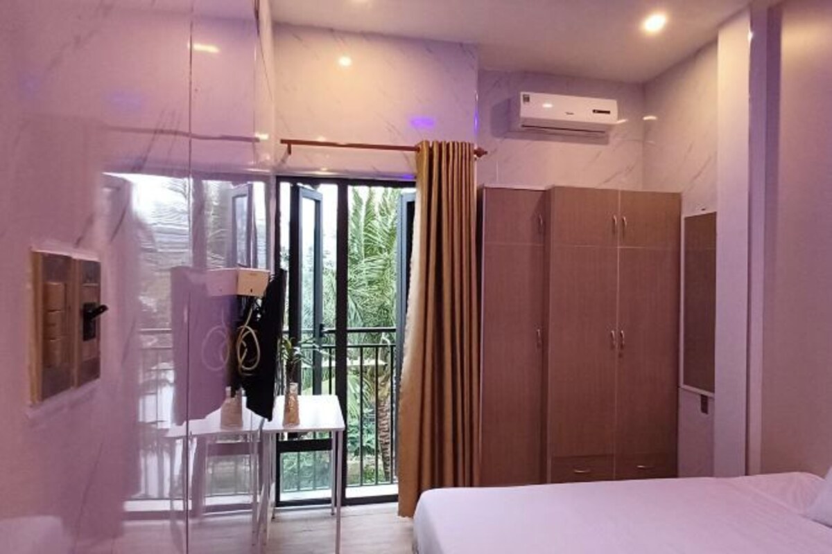 A modern hotel room with a bed, a wardrobe, a desk with a chair, and a balcony with curtains.