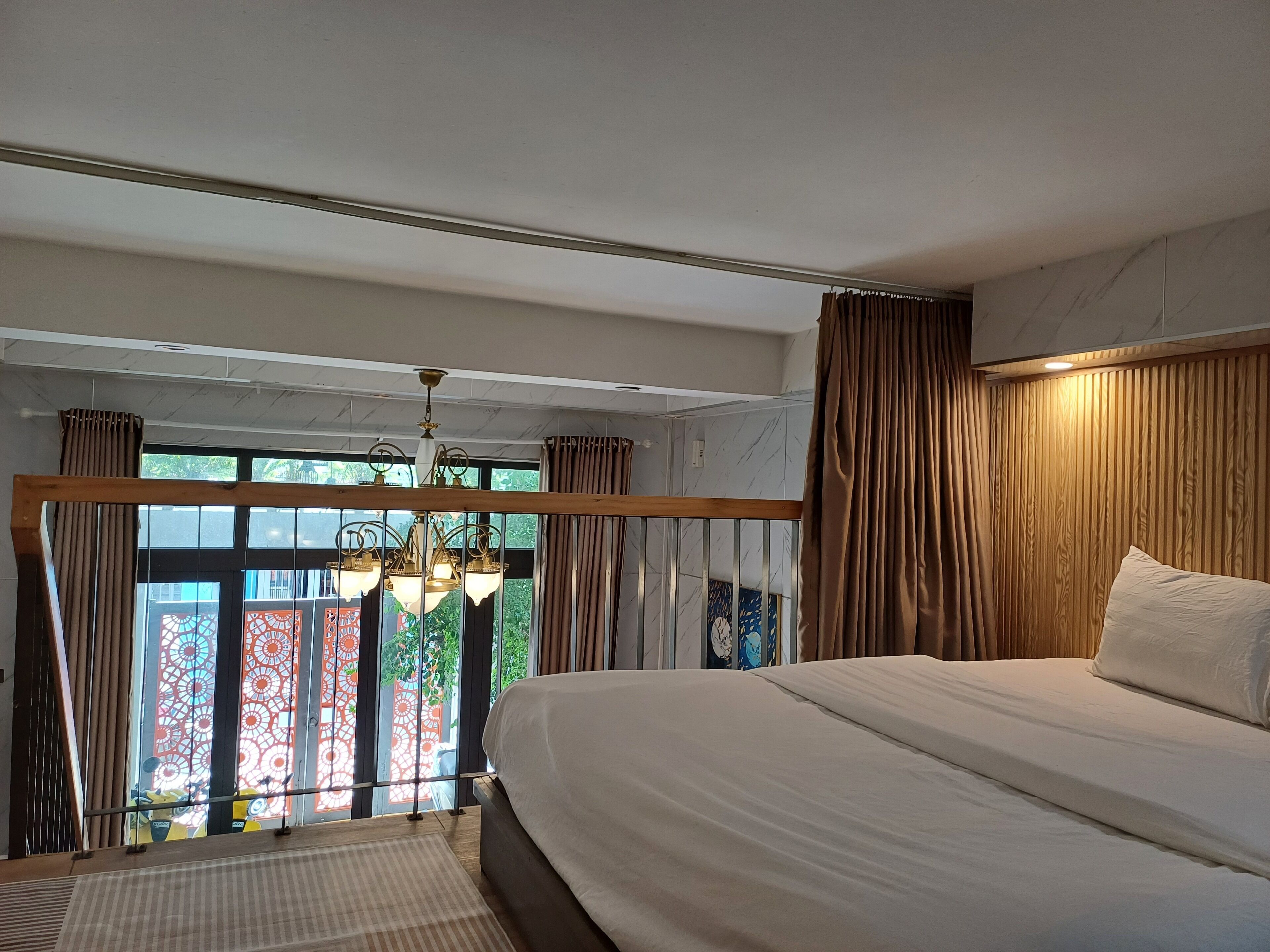 Een slaapkamer met een groot bed, een kroonluchter en uitzicht door een raam met gordijnen.