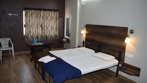Una habitación de hotel con cama, mesitas de noche, escritorio, silla y ventana con cortinas.