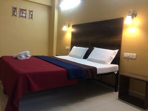 A hotel room with a bed, a red and blue blanket, a white pillow, and a wall-mounted light fixture. - Hotel Peacock (Hubli)