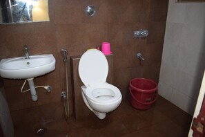 A bathroom with a white sink, a toilet, and a red bucket. - Hotel Peacock (Hubli)
