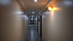 Un largo pasillo estrecho con piso oscuro y paredes claras, que presenta una serie de puertas y un accesorio de luz en la pared.