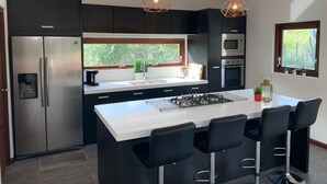 Une cuisine moderne dotée d’un îlot central, de tabourets de bar, d’appareils électroménagers en acier inoxydable et de luminaires suspendus.