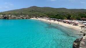 Une plage à l’eau turquoise et limpide, bordée d’un rivage sablonneux, avec, en arrière-plan, des collines verdoyantes.
