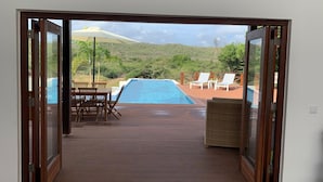Une terrasse ouverte avec une piscine, des meubles en bois et une vue sur une colline et un moulin à vent.