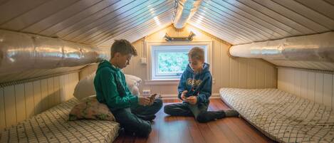 A small attic room with two beds, wooden floors, and a window with a view of trees.