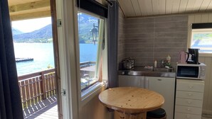 A compact kitchen with a wooden table and stools, a view of the sea, and a window with a curtain. - Fagervik Camping (Vestnes)