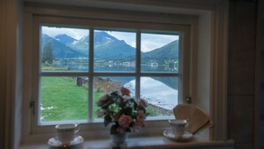 A room with a large window offering a view of a lake and mountains. - Fagervik Camping (Vestnes)