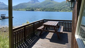 A wooden deck with a table and benches overlooking a lake with mountains in the background. - Fagervik Camping (Vestnes)