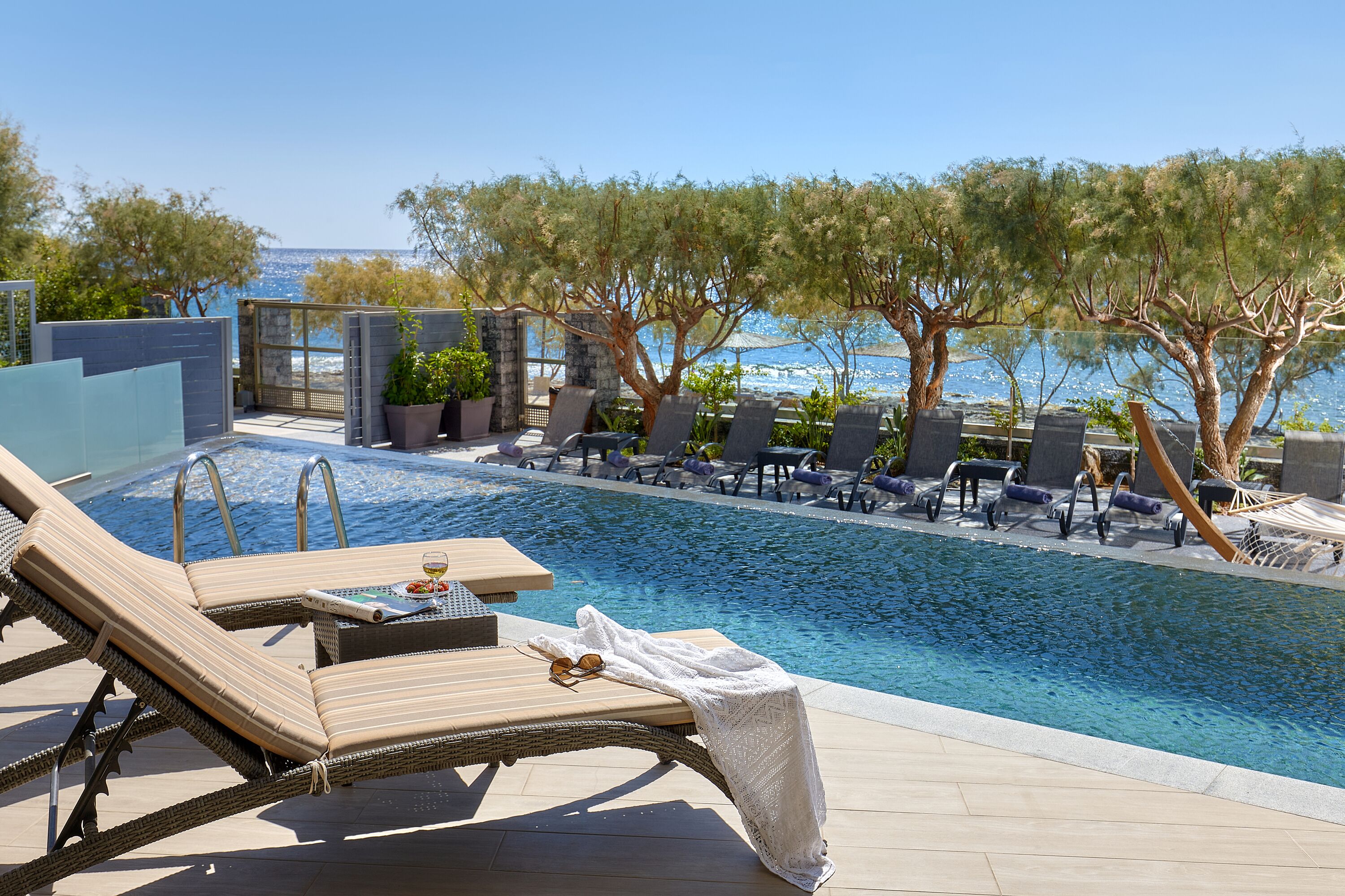 A poolside area with lounge chairs, a small table with a glass and a plate, and a view of the sea.