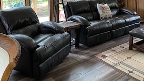 Ein geräumiges Wohnzimmer mit einer Ledersofa, einem Holztisch und Blick ins Freie durch große Fenster.