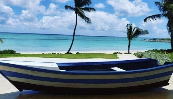 A boat on a beach with palm trees and a clear view of the ocean.