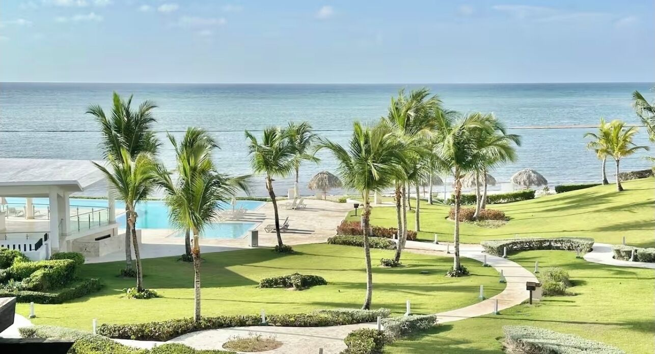 A resort with a pool, palm trees, and a view of the ocean.