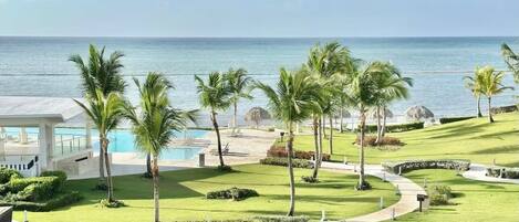 A resort with a pool, palm trees, and a view of the ocean.