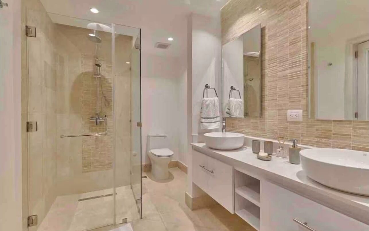 A modern bathroom with a glass shower enclosure, a toilet, and a double sink vanity with a large mirror.