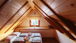 Une chambre mansardée chaleureuse avec un plafond en bois incliné, une petite fenêtre avec un rideau et un lit agrémenté de serviettes roulées.