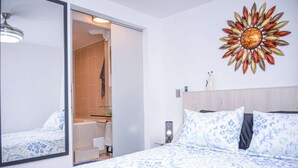 A bedroom with a bed, a large mirror, a sunburst wall decoration, and a visible bathroom with a shower.