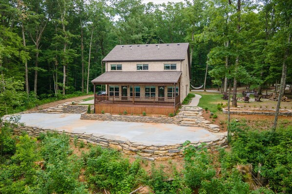 A two-story house with a stone deck and a covered porch, surrounded by dense forest. - Beautiful Monteagle Bluff Mountain Home Sleeps 12 (Monteagle)