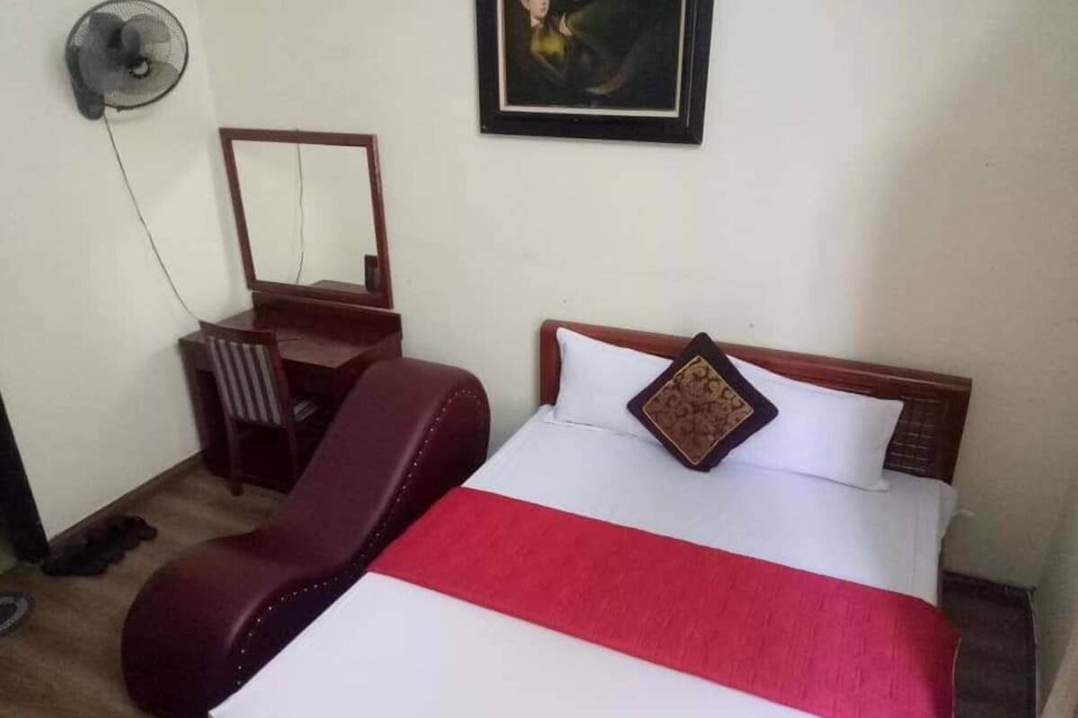 Una habitación de hotel con una cama, un escritorio, una silla y un ventilador de pared.