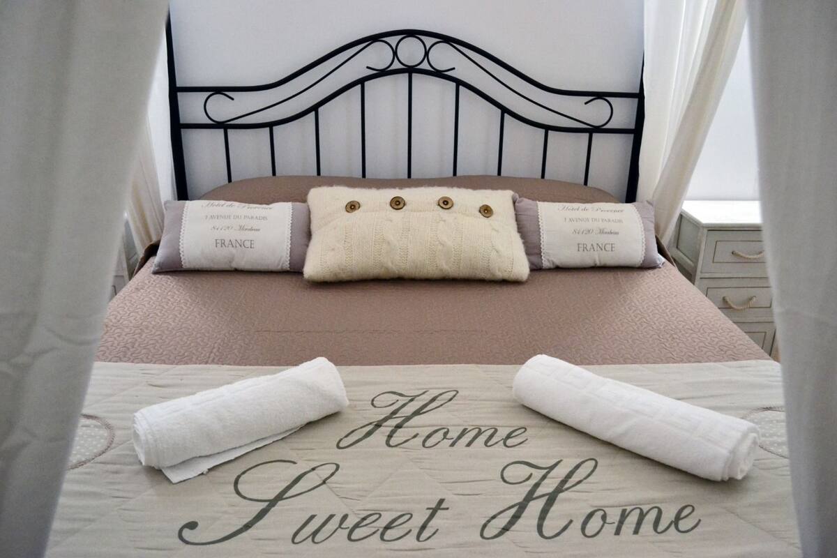 Una cama bien hecha con cabecera, almohadas y una manta. El edredón tiene el texto 'Home Sweet Home' impreso.