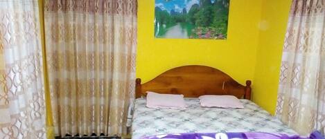 Un dormitorio con cama, cortinas, un cuadro y una alfombra pequeña.