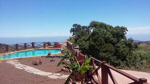 Una piscina con vistas claras al océano, rodeada por una valla de madera y un camino de piedra.