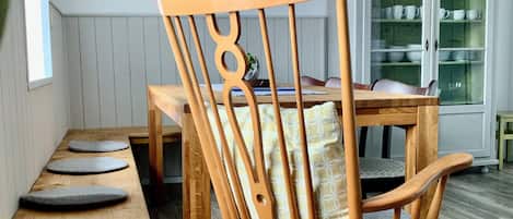 Una mecedora de madera con un cojín, un banco de madera y una mesa de comedor con sillas.
