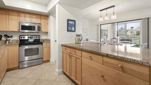 Une cuisine moderne dotée d’appareils électroménagers en acier inoxydable, de meubles en bois et d’une grande fenêtre offrant une vue sur l’extérieur.