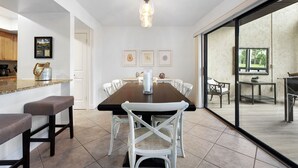 Un coin repas avec une table en bois foncé, des chaises blanches et un vase en verre servant de centre de table.