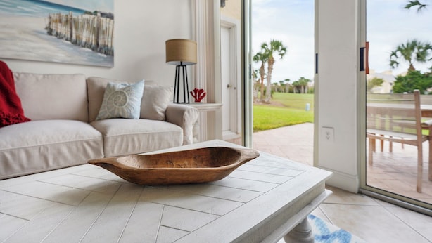 Un salon moderne avec une grande fenêtre, un bol en bois posé sur une table, un canapé avec des coussins et un tableau accroché au mur.