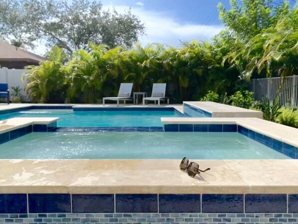 A swimming pool with two lounge chairs and a bird on the edge.