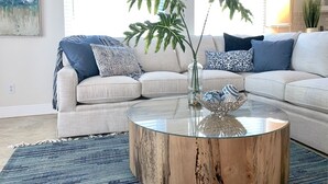 A living room with a beige sectional sofa, a round coffee table, and a large plant. - New Resort style Pool/Spa minutes to Vanderbilt beach! BlueBeachBungalow1 (Naples)