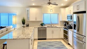 A modern kitchen with white cabinets, stainless steel appliances, and a ceiling fan. - New Resort style Pool/Spa minutes to Vanderbilt beach! BlueBeachBungalow1 (Naples)