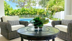A patio area with wicker furniture, a round table, and a view of a swimming pool and greenery. - New Resort style Pool/Spa minutes to Vanderbilt beach! BlueBeachBungalow1 (Naples)