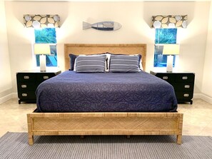 A bedroom with a wooden bed frame, a dark blue bedspread, two bedside tables with lamps, and wall art including a fish and abstract designs.