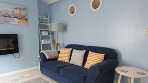 Ein Wohnzimmer mit einem blauen Sofa, einem kleinen runden Tisch, einem Fernseher und einem Bild an der Wand.