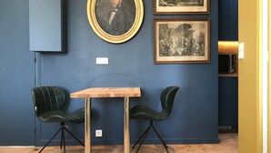 Una habitación con pared azul, una mesa de madera, dos sillas verdes y dos cuadros blanco y negro enmarcados.