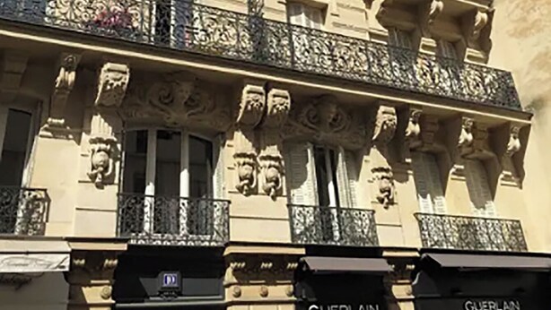 Un edificio de varios pisos con detalles arquitectónicos ornamentales, incluyendo estatuas y molduras decorativas.