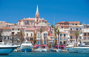Un puerto deportivo con barcos amarrados, una iglesia destacada con un campanario alto y edificios con techos de tejas rojas.
