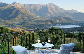Un balcón con una mesa y dos sillas, con vistas a un paisaje montañoso y un lago.