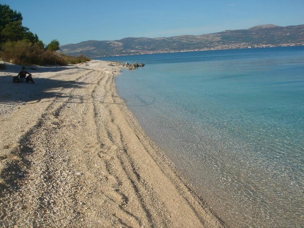 A beach with clear water and a person sitting on the sand.