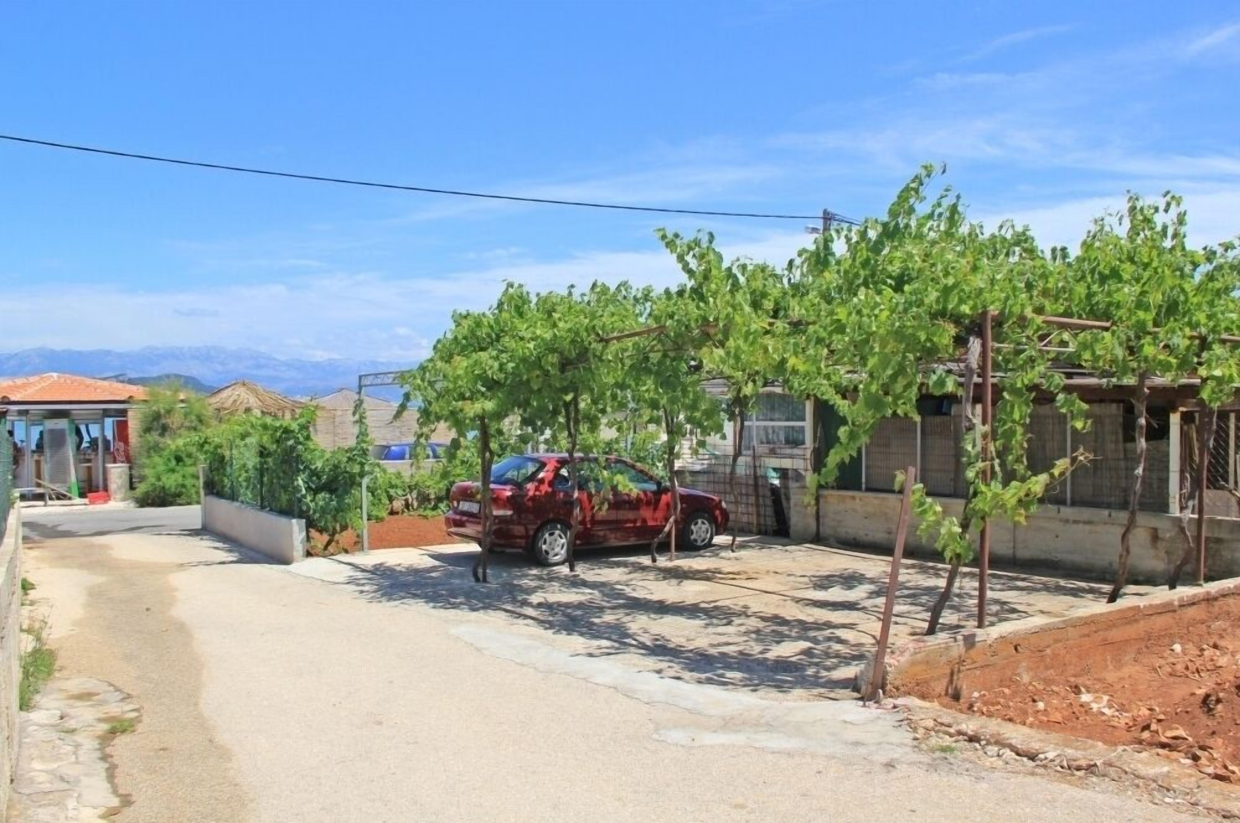 A red car parked on a paved driveway with a vineyard in the background.