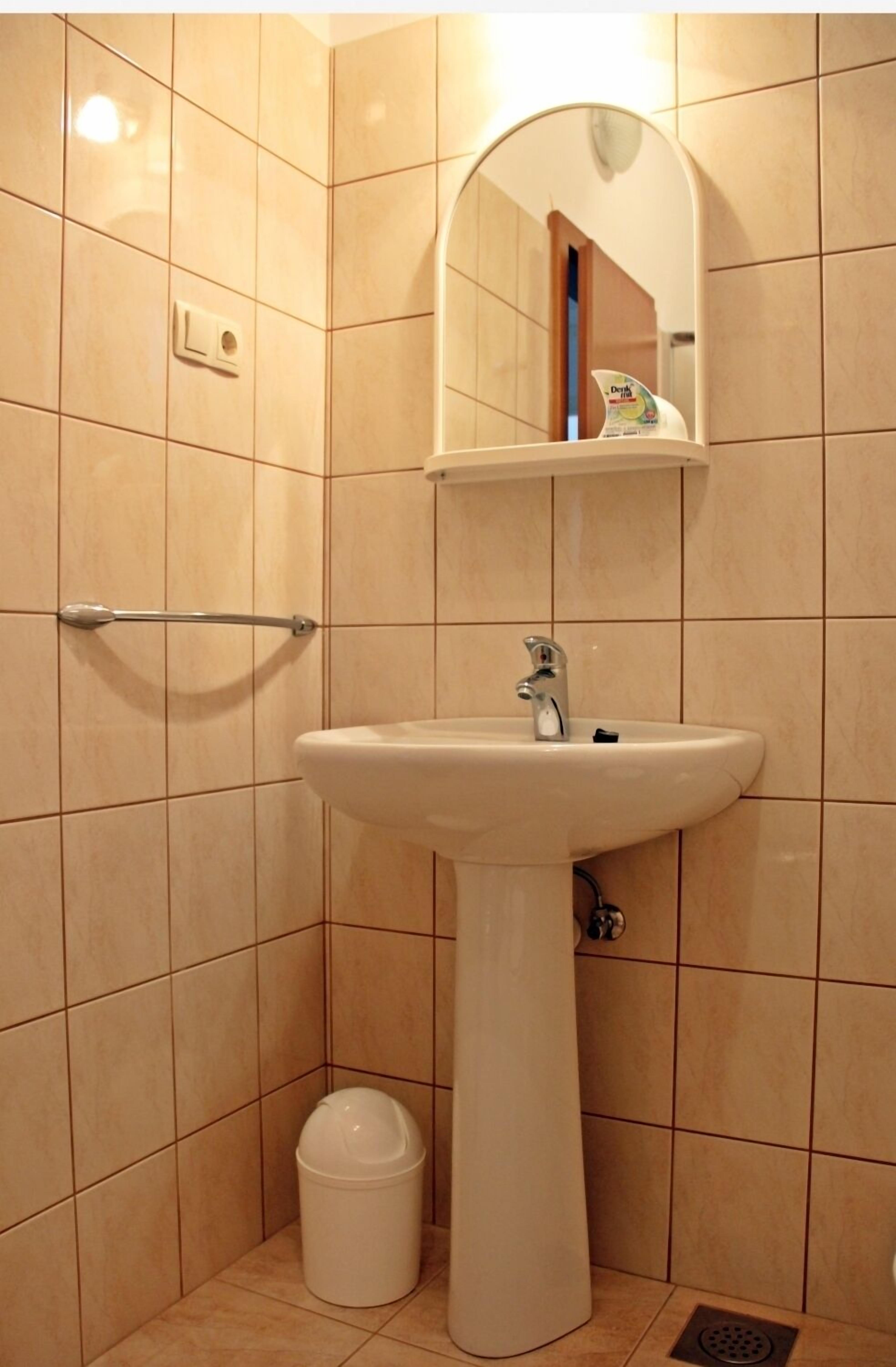 A bathroom with a pedestal sink, a mirror, a towel rack, and a waste bin.