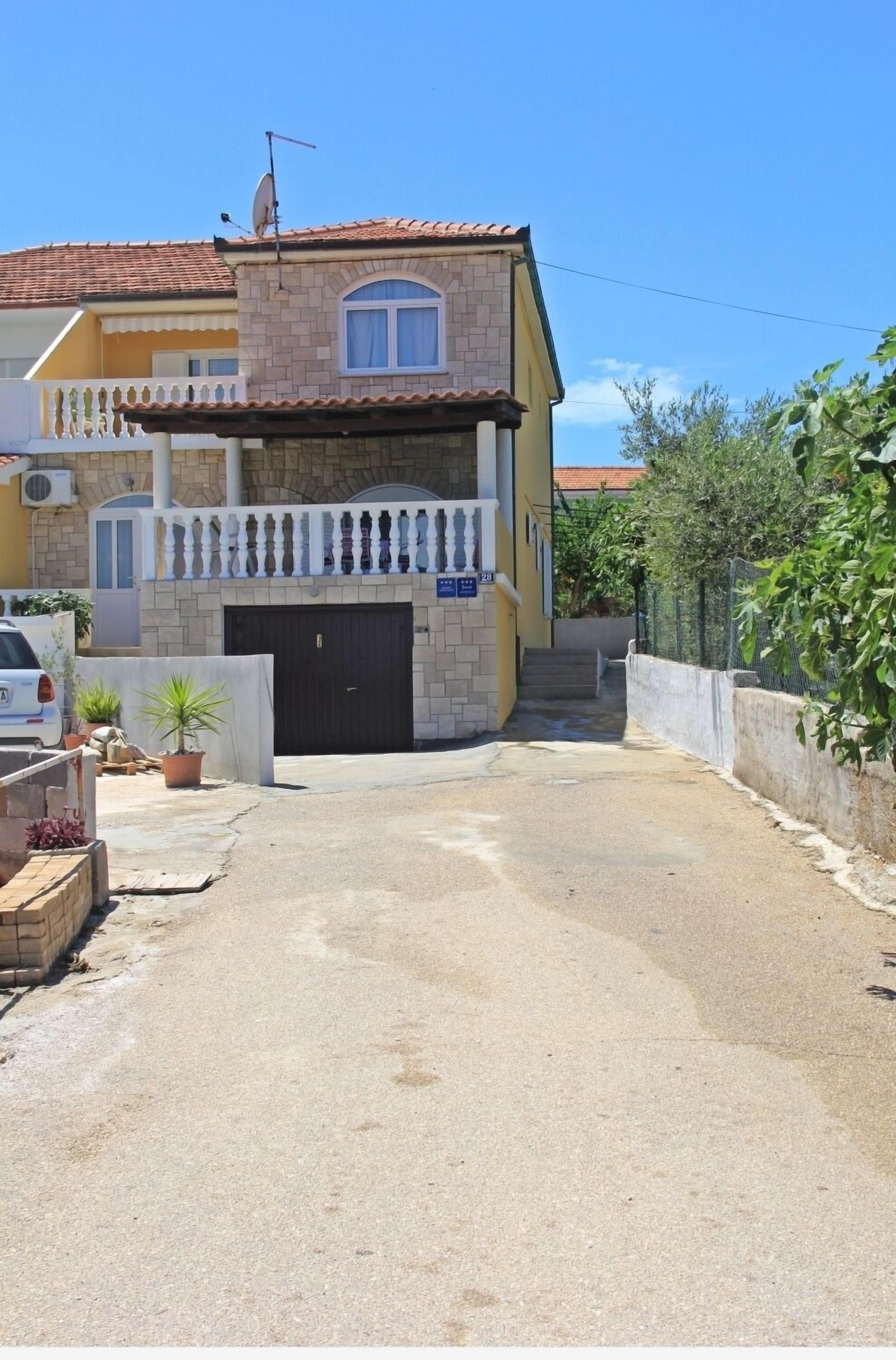 A two-story building with a tiled roof, a balcony with white railings, and a black garage door.