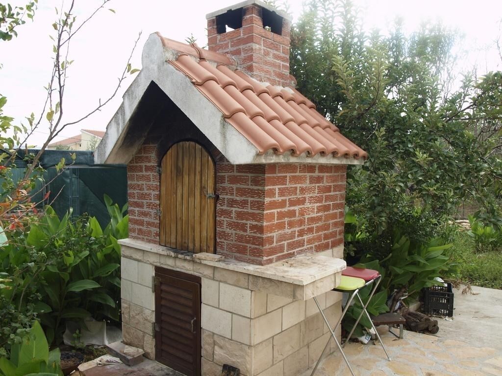 Een gebouwd buitenbouwobject van baksteen met een pannendak, een houten deur en een klein zitgedeelte.