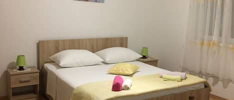 A bedroom with a wooden bed, white bedding, a green lamp on the nightstand, and a painting on the wall.